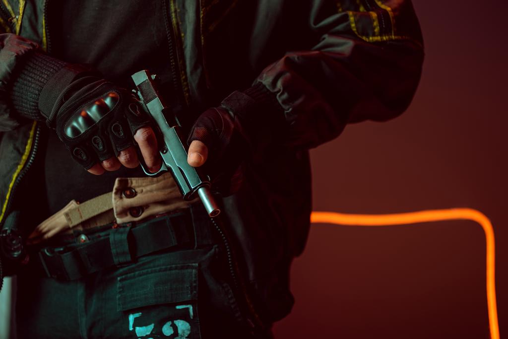 cropped άποψη του οπλισμένου παίκτη cyberpunk με όπλο στο μαύρο με φωτισμό νέον  - Φωτογραφία, εικόνα
