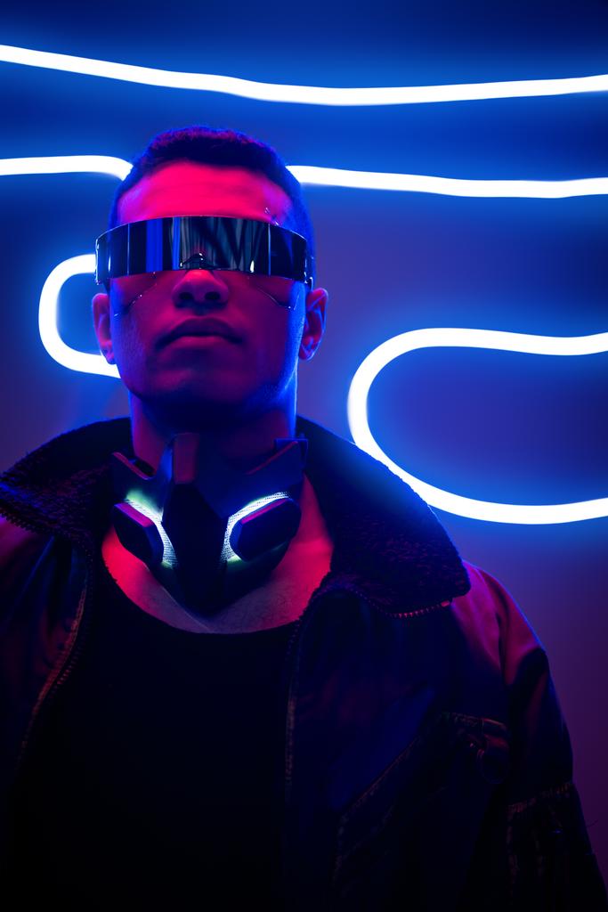 Cyberpunk-Mixed-Race-Spieler mit futuristischer Brille in der Nähe von Neonbeleuchtung  - Foto, Bild