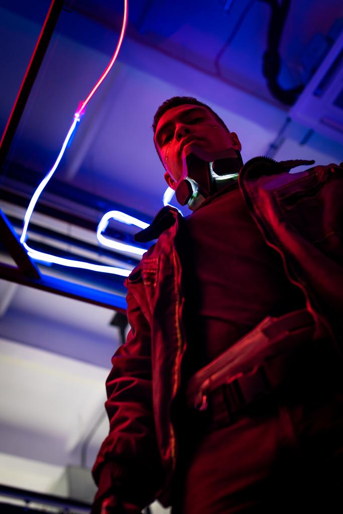 άποψη χαμηλής γωνίας του bi-φυλετικού cyberpunk player στέκεται κοντά σε μπλε νέον φωτισμό  - Φωτογραφία, εικόνα
