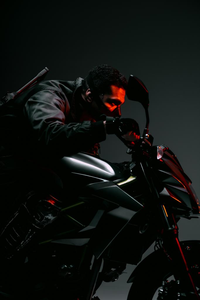 вид збоку збройного дворасового кіберпанку в масці їзда на мотоциклі на сірому
  - Фото, зображення