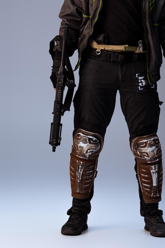 Обрезанный вид киберпанка, держащего в руках пистолет и стоящего на сером
   - Фото, изображение