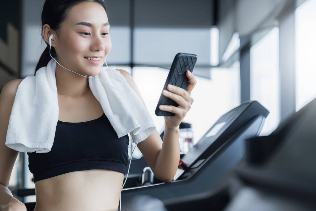 zdravá asijská žena ve sportovním oblečení relaxovat a vychutnat píseň z chytrého telefonu po cvičení v tělocvičně - Fotografie, Obrázek
