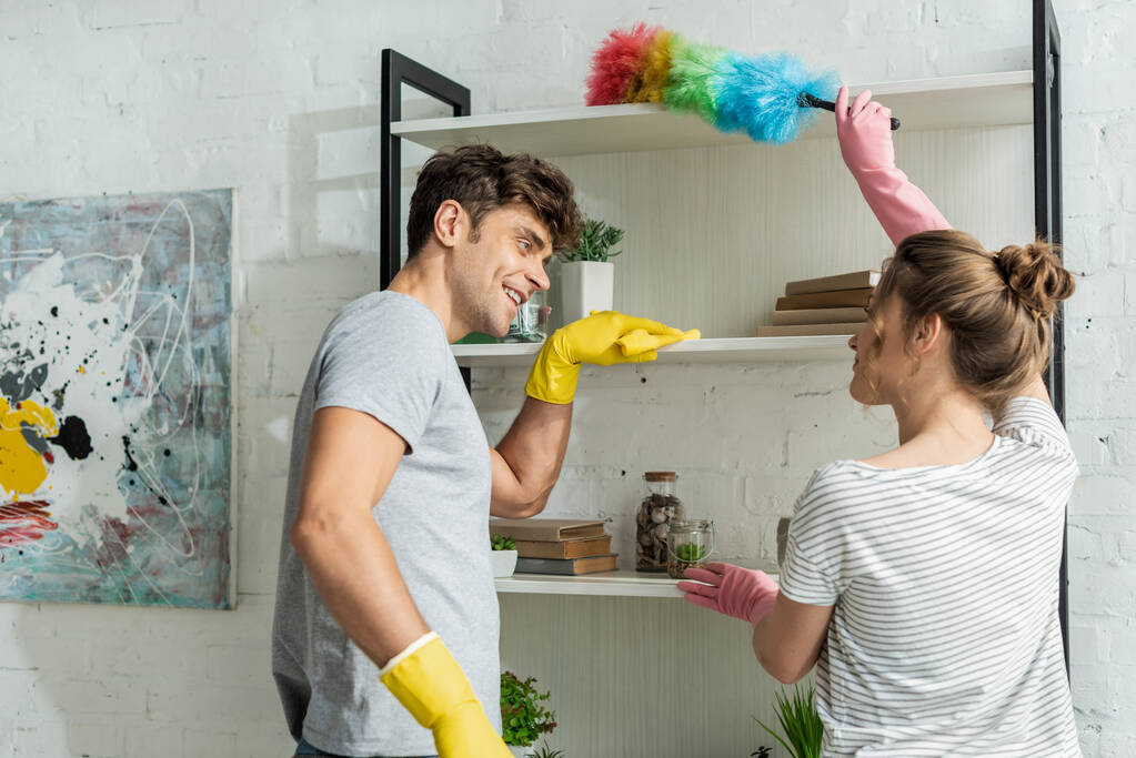Selektiver Fokus glücklicher Mädchen und Männer beim Reinigen von Regalen zu Hause  - Foto, Bild