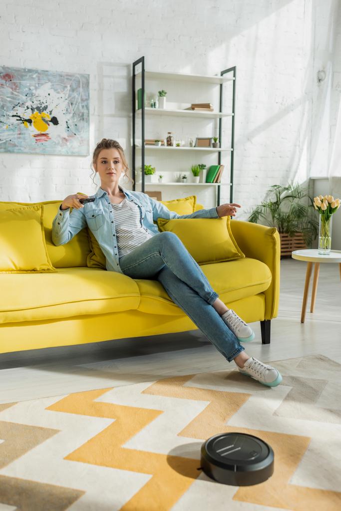 giovane donna guardando la tv mentre robot aspirapolvere tappeto di lavaggio in soggiorno
  - Foto, immagini