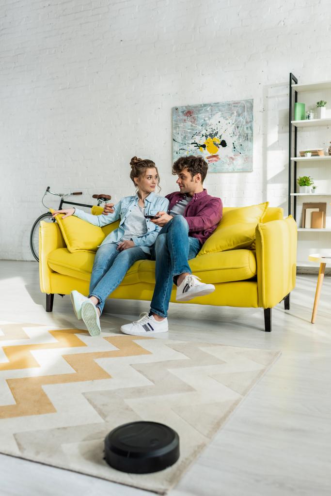 счастливый мужчина и женщина смотрят кино в то время как роботизированный пылесос стиральный ковер в гостиной
  - Фото, изображение