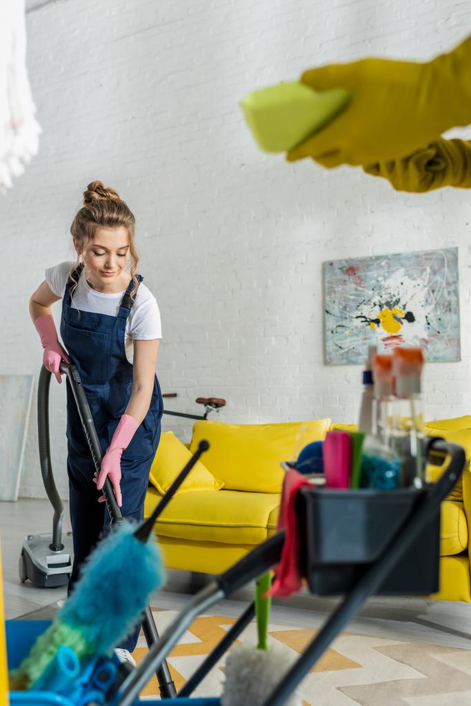 selective focus of attractive cleaner using vacuum cleaner near coworker with sponge  - Photo, Image