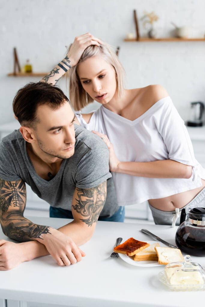 Selective focus of tattooed couple near toasts and coffee on kitchen table  - Photo, Image