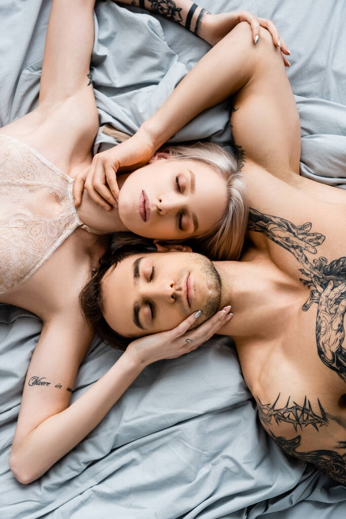 Κάτοψη του ζευγαριού με τα τατουάζ με κλειστά μάτια να αγγίζονται στο κρεβάτι  - Φωτογραφία, εικόνα