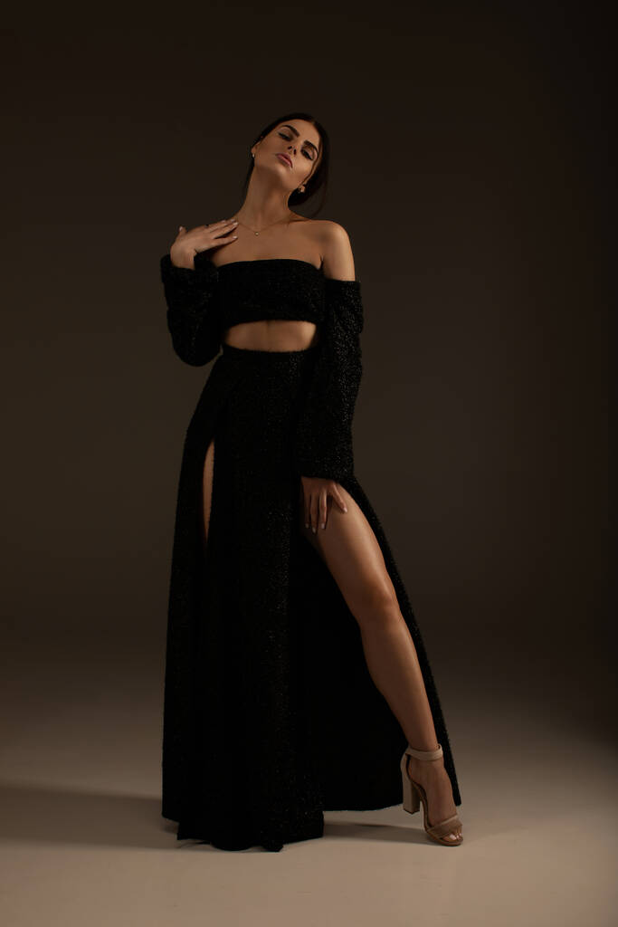 Élégante belle femme aux longues jambes en robe noire à la mode posant en studio sur fond gris
. - Photo, image
