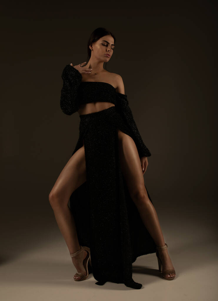 Elegante bella donna con lunghe gambe in abito nero alla moda in posa in studio su sfondo grigio
. - Foto, immagini