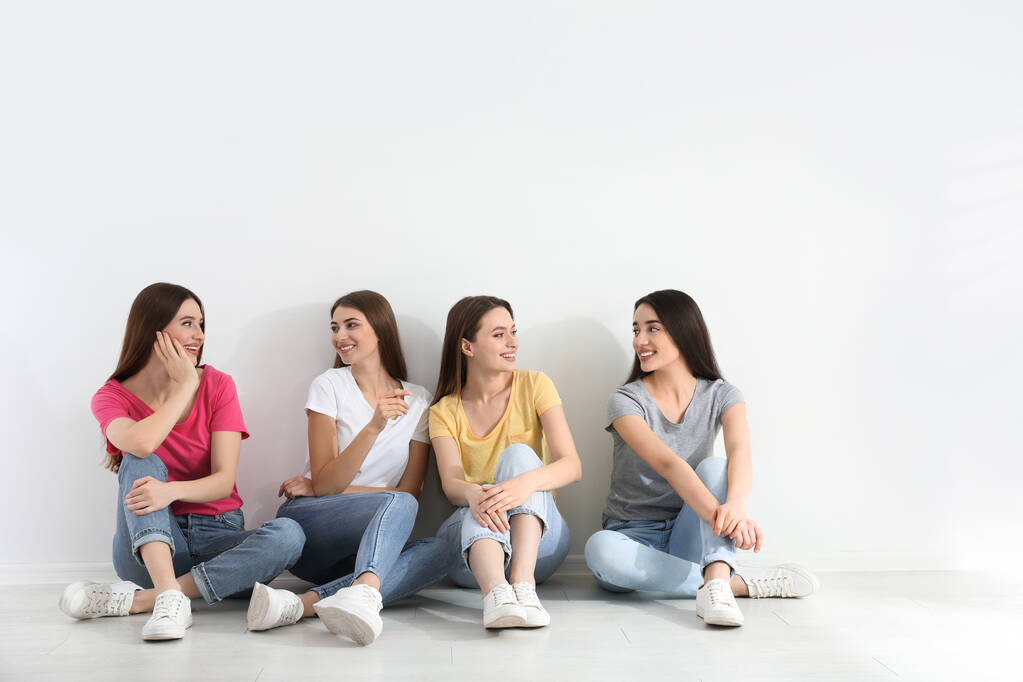 Красивые юные леди в джинсах и разноцветных футболках возле белой стены в помещении. Женский день
 - Фото, изображение