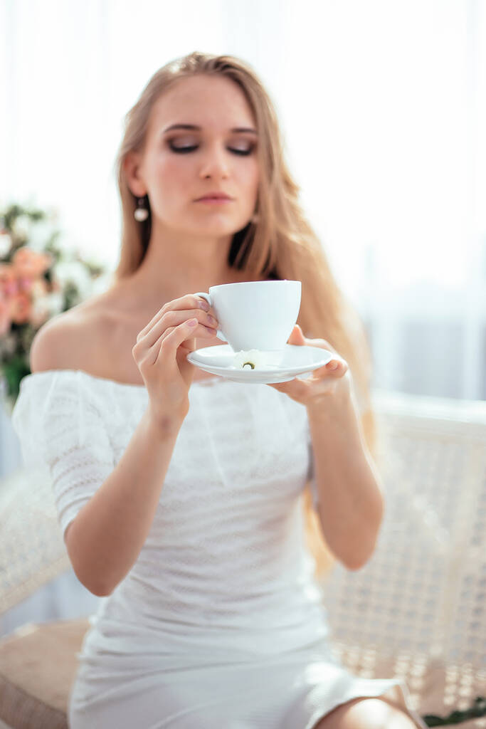 女の子は朝のお茶を飲み、人生を楽しんで、花の花束、日当たりの良い光を賞賛します. - 写真・画像