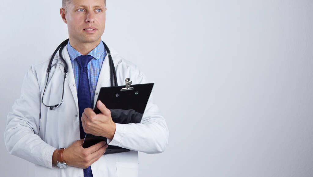 Мужчина врач стоя с папкой, изолированные на белом фоне - Фото, изображение