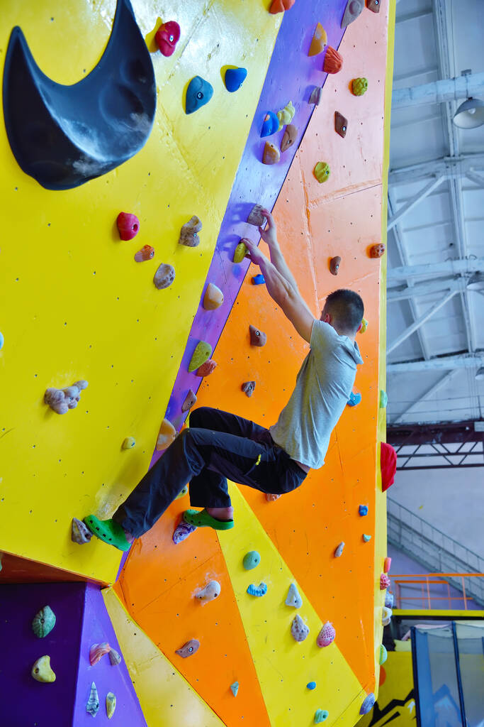 ジムで練習用の壁に登っている若い男。極端な健康的なライフスタイルの概念. - 写真・画像