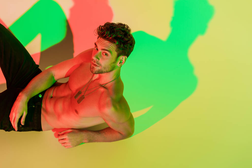сексуальний, без сорочки чоловік дивиться на камеру, лежачи на жовтому з червоними і зеленими тінями
 - Фото, зображення