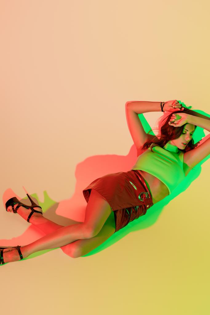 top view of attractive, trendy girl lying with closed eyes on yellow background with green and red shadows - Photo, Image