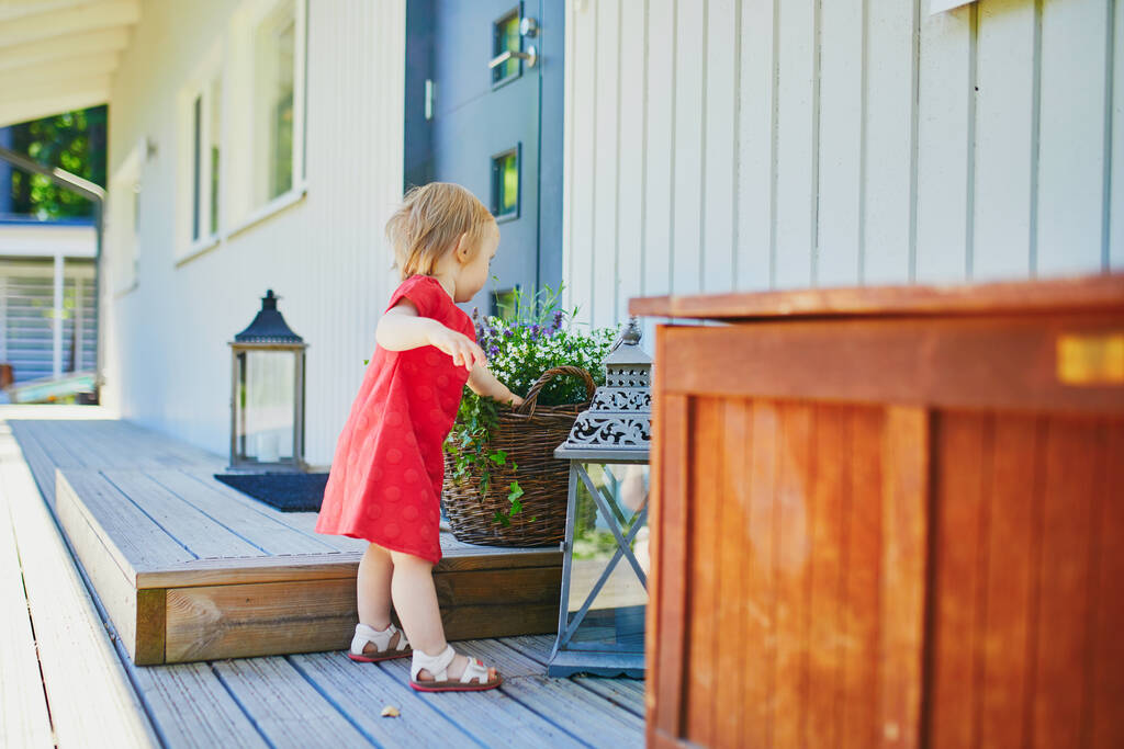 Чарівна дівчинка в червоній сукні розважається на відкритому повітрі на її домашній терасі в сонячний літній день
 - Фото, зображення