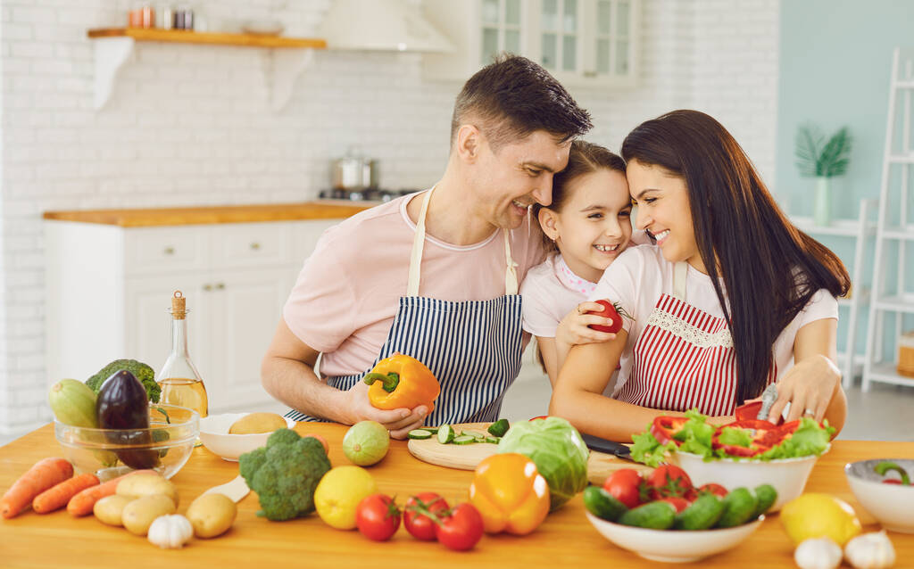 Ευτυχισμένη οικογένεια με κόρη στην κουζίνα με λαχανικά. - Φωτογραφία, εικόνα