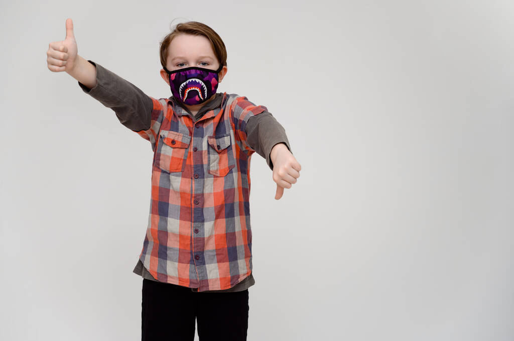 Круте фото 9-річного хлопчика-підлітка у масці та сорочки на білому тлі. Модель вказує пальці на сторони
. - Фото, зображення