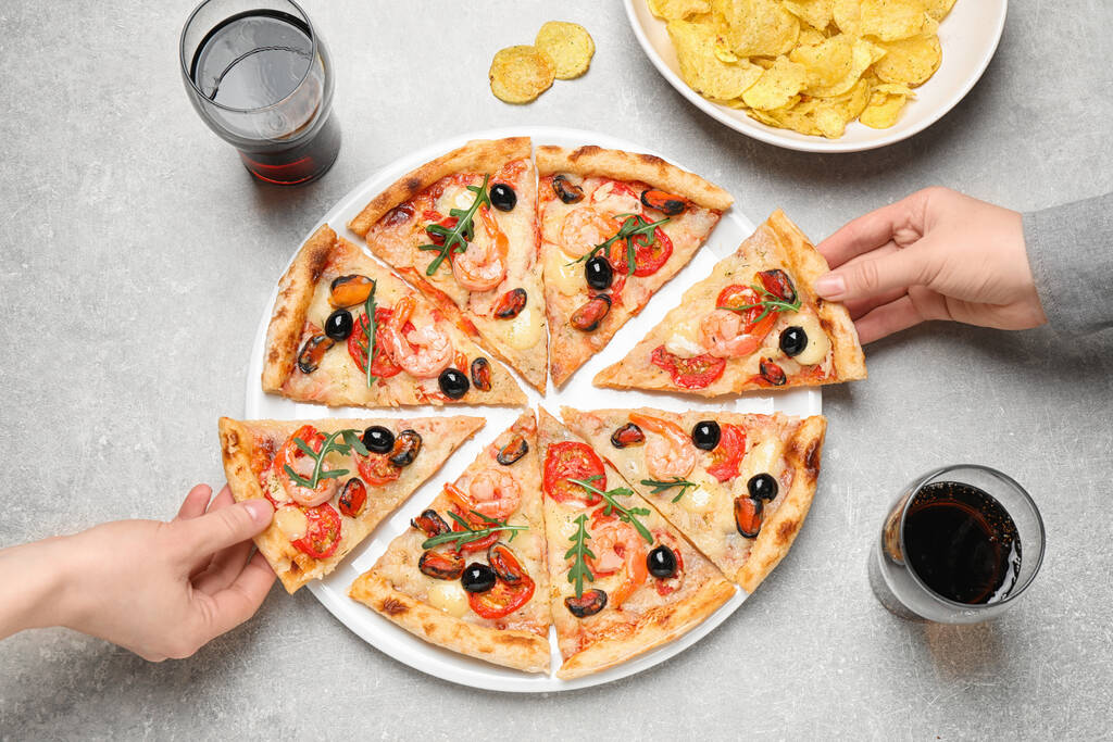 Mensen nemen plakjes lekkere pizza met zeevruchten aan lichtgrijze tafel, bovenaanzicht - Foto, afbeelding