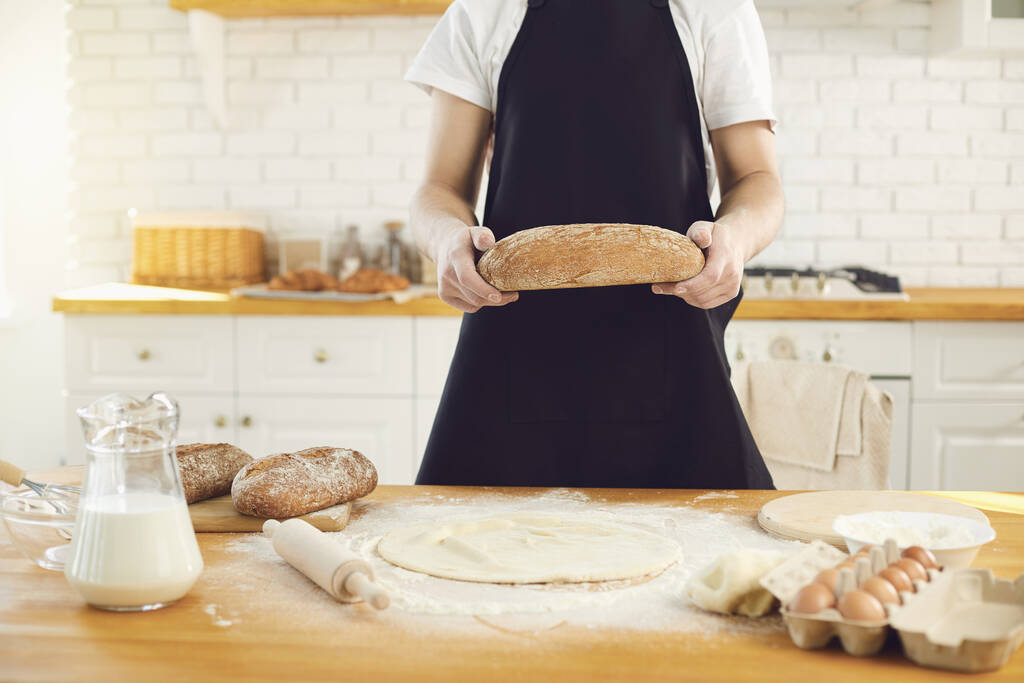 Baker homme barbu homme tient dans ses mains du pain frais debout dans la cuisine
. - Photo, image
