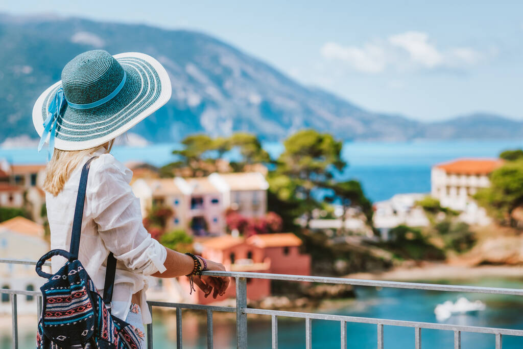 Turisti nainen yllään sininen aurinko hattu nauttia ylhäältä näkymä värikäs rauhallinen kylä Assos aurinkoisena päivänä. Vierailu Kefalonia, Kreikka kesällä matka loma
 - Valokuva, kuva
