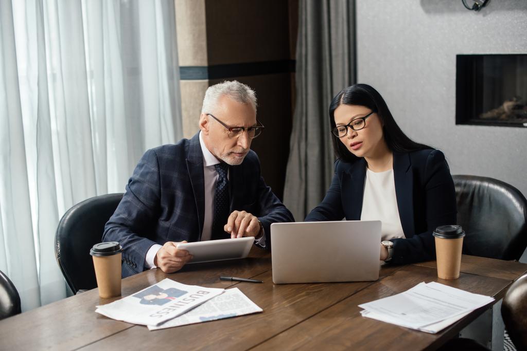 бизнесмен и азиатская деловая женщина смотрит на ноутбук и разговаривает во время деловой встречи
  - Фото, изображение
