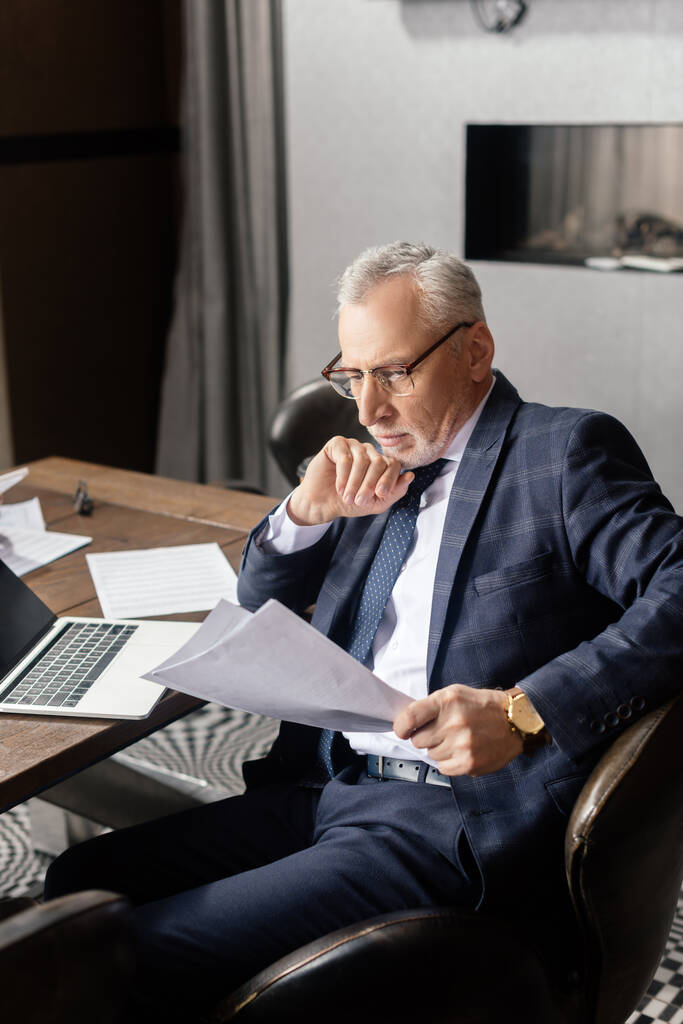 focused businessman sitting at table and doing paperwork in hotel  - Photo, Image