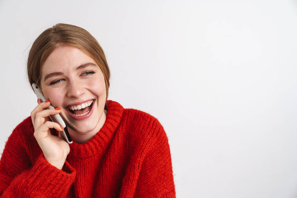 Kuva iloinen nuori nainen poseeraa yli valkoinen seinä tausta puhuu matkapuhelimella
. - Valokuva, kuva