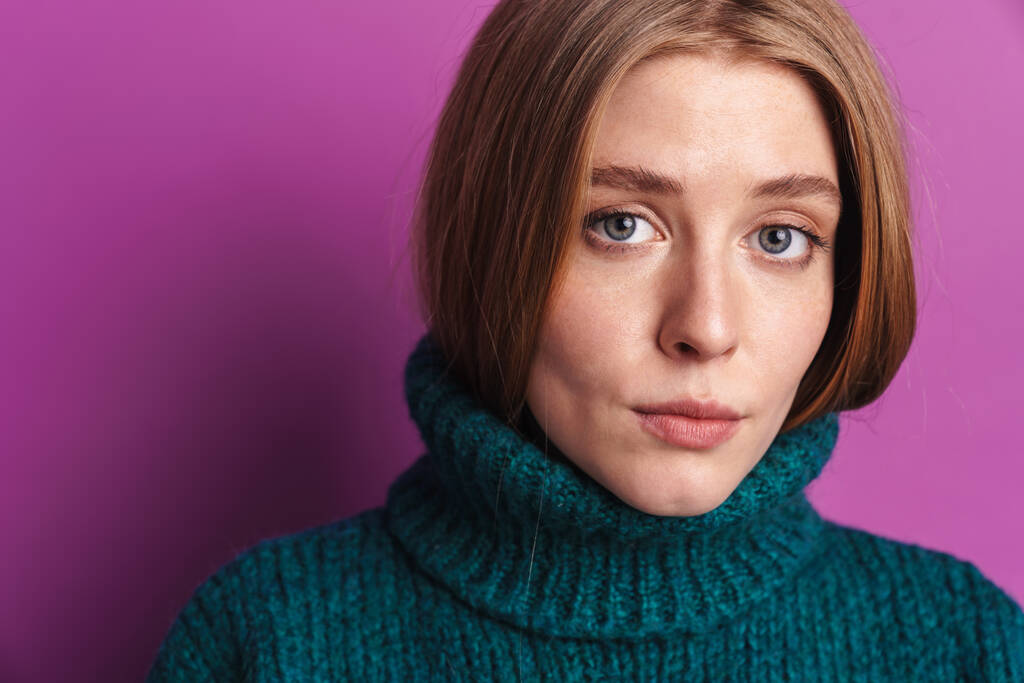 Photo of calm caucasian woman in green sweater posing and looking at camera isolated over violet wall - Photo, Image