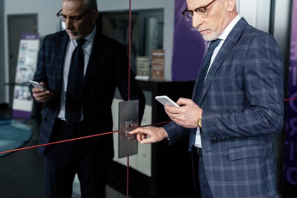 oříznutý pohled na podnikatele pomocí chytrého telefonu a stisknutím tlačítka výtahu  - Fotografie, Obrázek