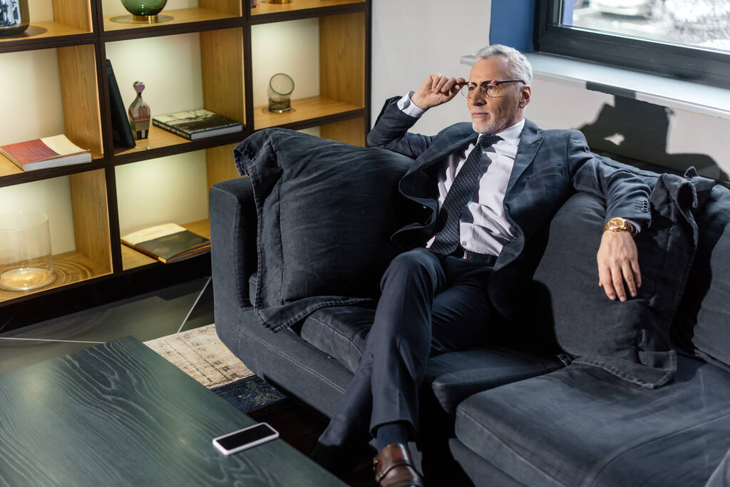 Blick aus der Vogelperspektive: Geschäftsmann im Anzug sitzt auf Sofa und schaut weg  - Foto, Bild