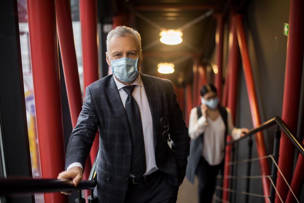 biznesmen w garniturze z maską medyczną patrzący przed kamerą  - Zdjęcie, obraz