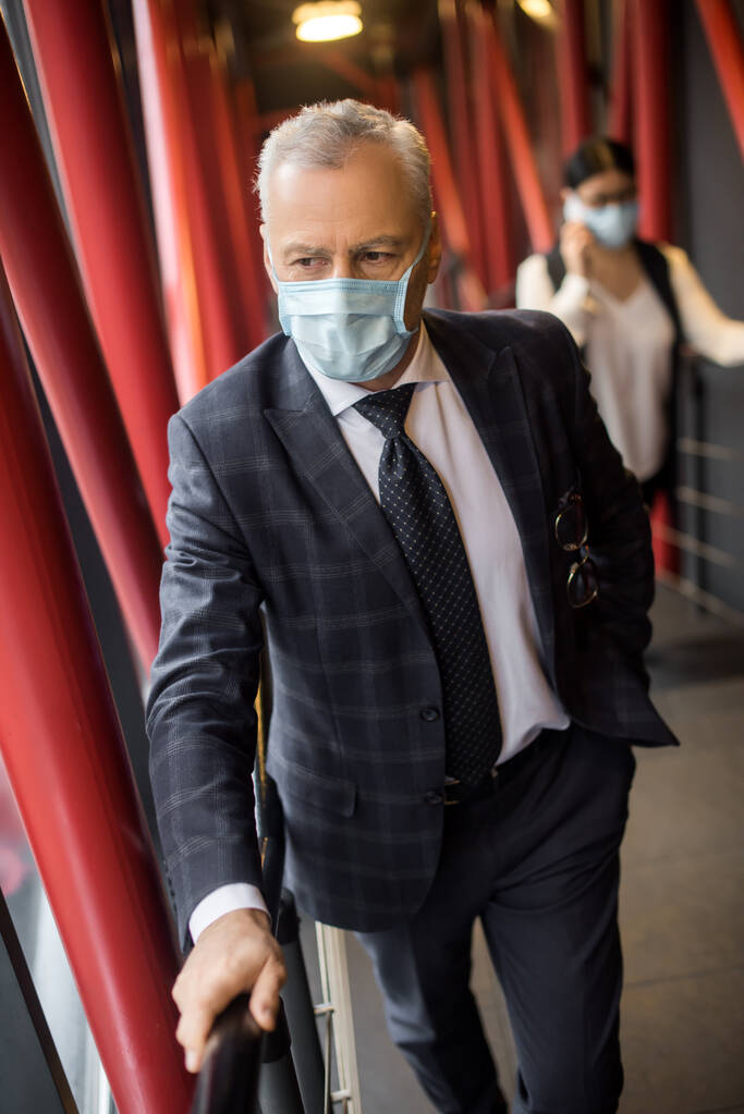 бізнесмен в офіційному одязі з медичною маскою, дивлячись подалі
  - Фото, зображення