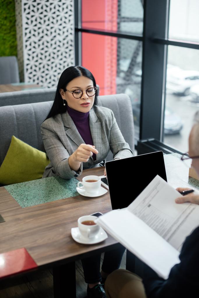 избирательный фокус азиатской предпринимательницы, указывающей пальцем на бумагу и беседующей с бизнесменом
 - Фото, изображение