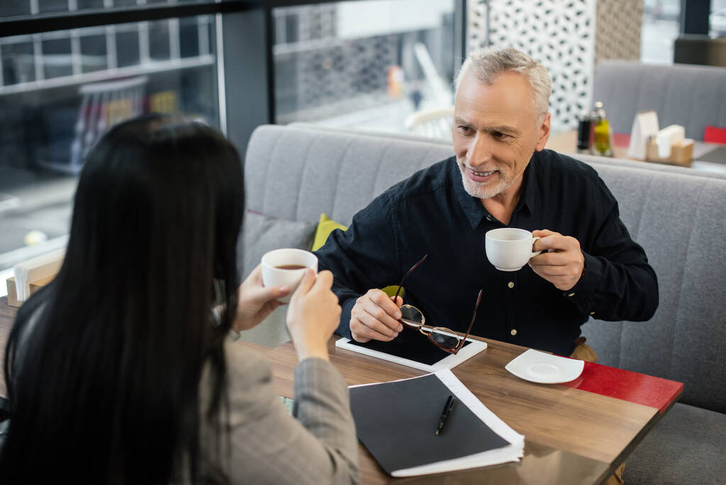 szelektív fókusz mosolygós üzletember tartó csésze és beszél üzletasszony a kávézóban  - Fotó, kép