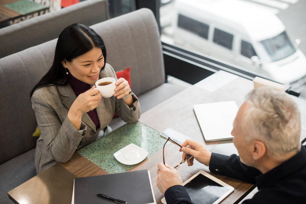 high angle view of businessman and asian businesswoman with cup talking in cafe  - Photo, Image