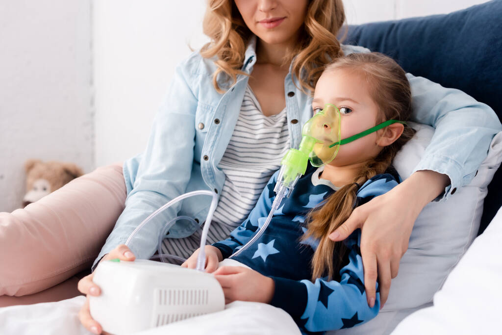 圧縮機吸入器を使って呼吸マスクの娘と座っている母親は  - 写真・画像