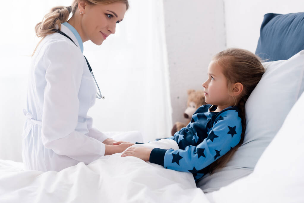 ελκυστικός γιατρός με λευκό παλτό κοιτάζοντας άρρωστο παιδί  - Φωτογραφία, εικόνα