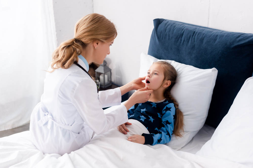 attraktive Ärztin im weißen Kittel untersucht krankes Kind  - Foto, Bild