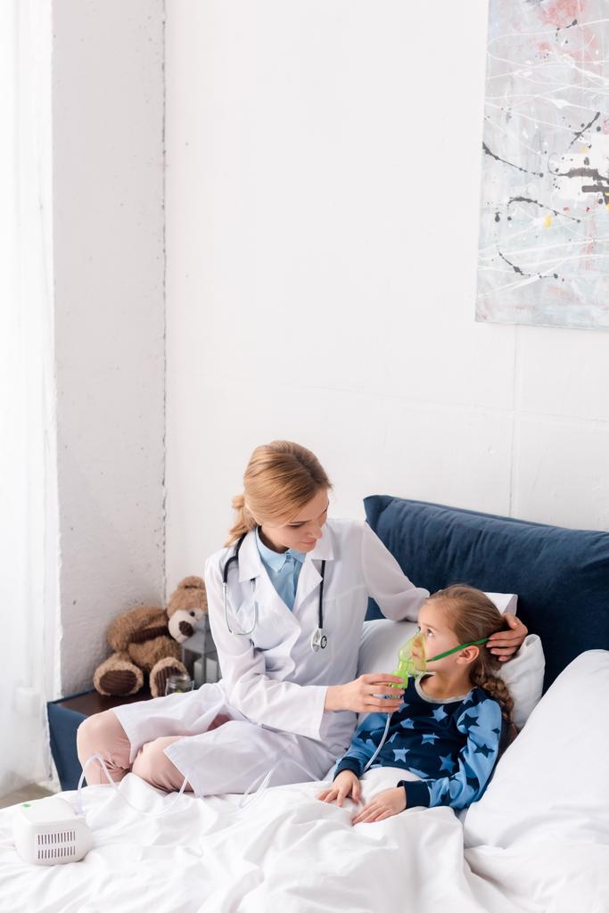 vonzó orvos fehér köpenyben megható légzőszervi maszk asztmás gyermek  - Fotó, kép