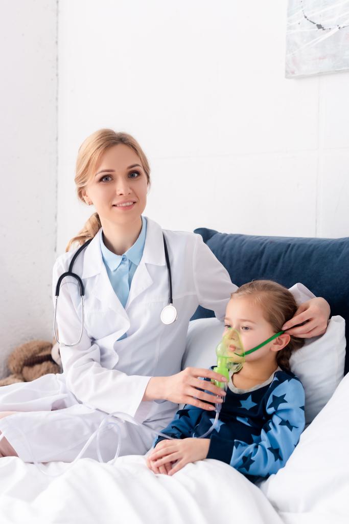 красивый доктор в белом халате трогает респираторную маску на больном ребенке
  - Фото, изображение