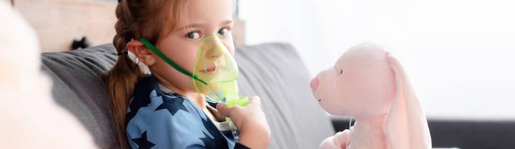 柔らかいおもちゃの近くの呼吸マスクを使用して喘息の子供のパノラマショット  - 写真・画像