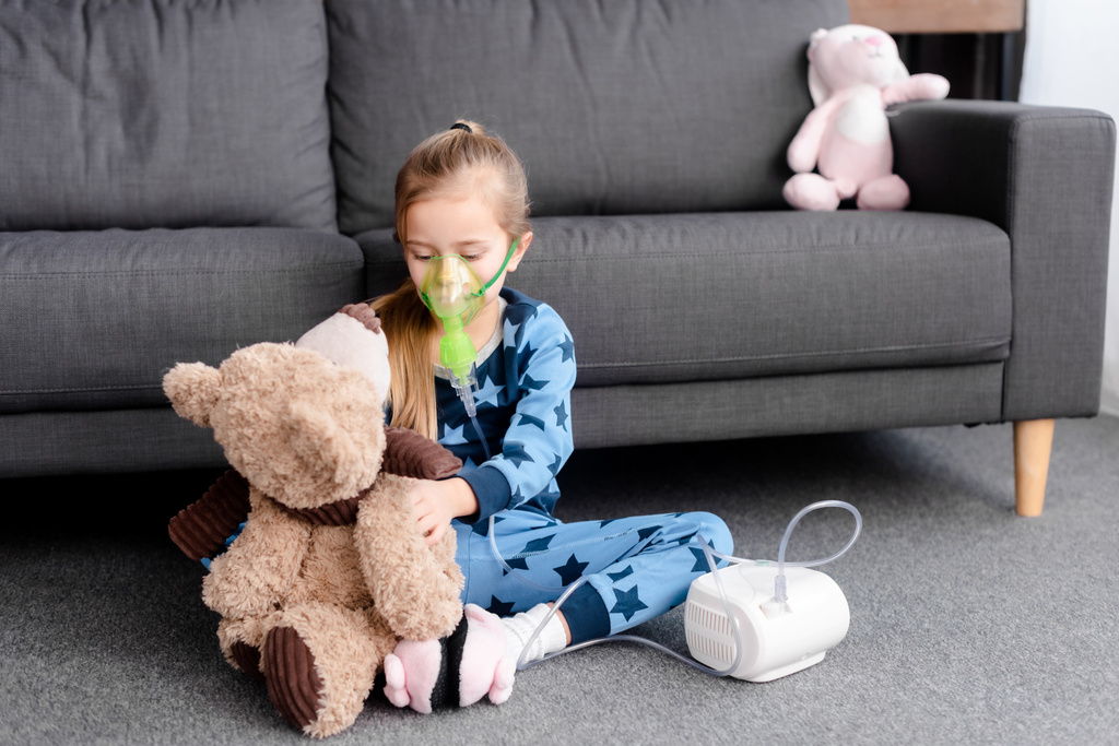 criança asmática usando inalador compressor e segurando ursinho de pelúcia
  - Foto, Imagem
