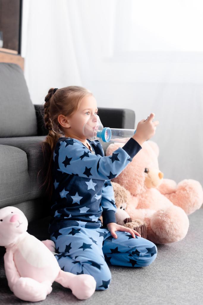 criança doente usando inalador com espaçador perto de brinquedos macios
 - Foto, Imagem