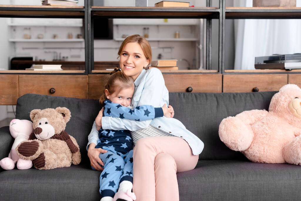 cute kid hugging mother near soft toys on sofa  - Photo, Image
