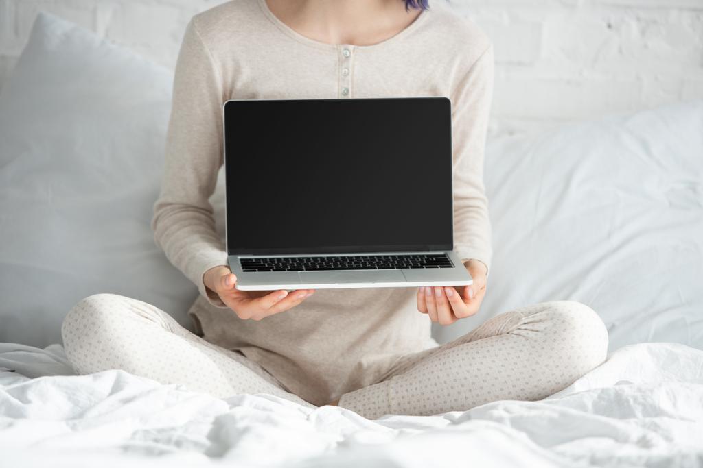 Vista cortada de freelancer com cabelo colorido e pernas cruzadas mostrando laptop na cama no quarto
 - Foto, Imagem