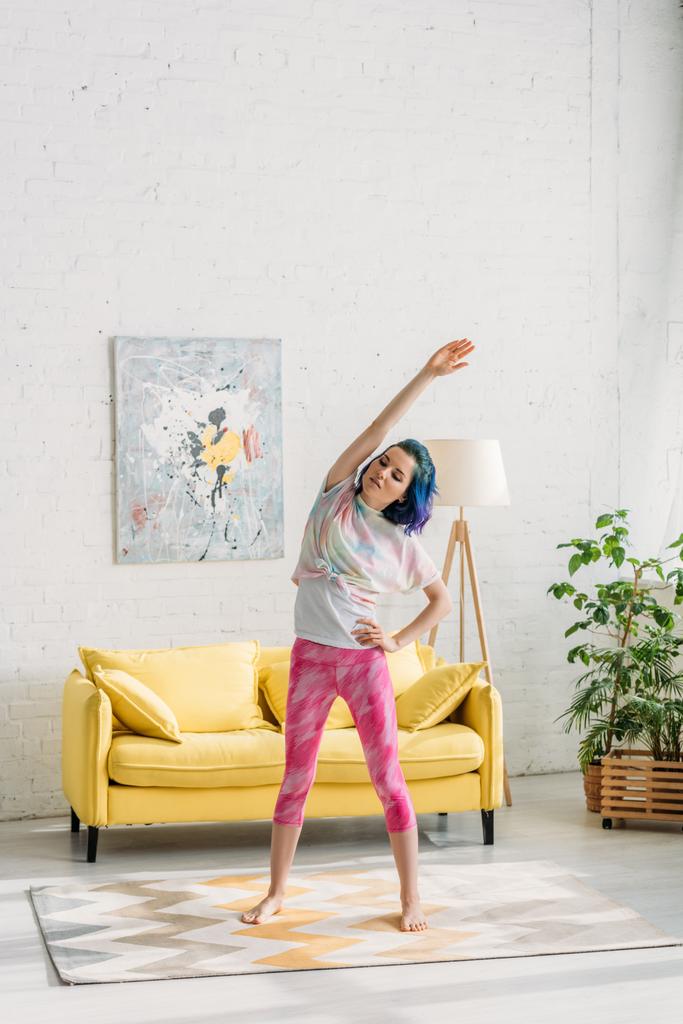 Chica con el pelo colorido calentamiento con la mano en la cadera en la sala de estar
 - Foto, imagen