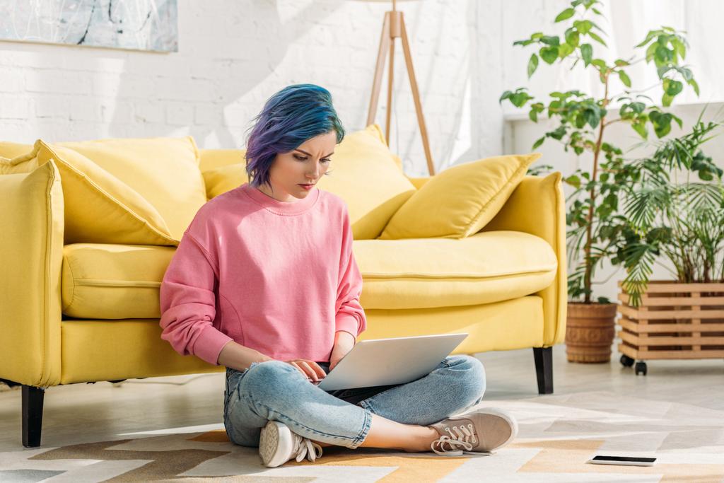 Freelancer com cabelo colorido trabalhando com laptop perto de smartphone no chão
  - Foto, Imagem