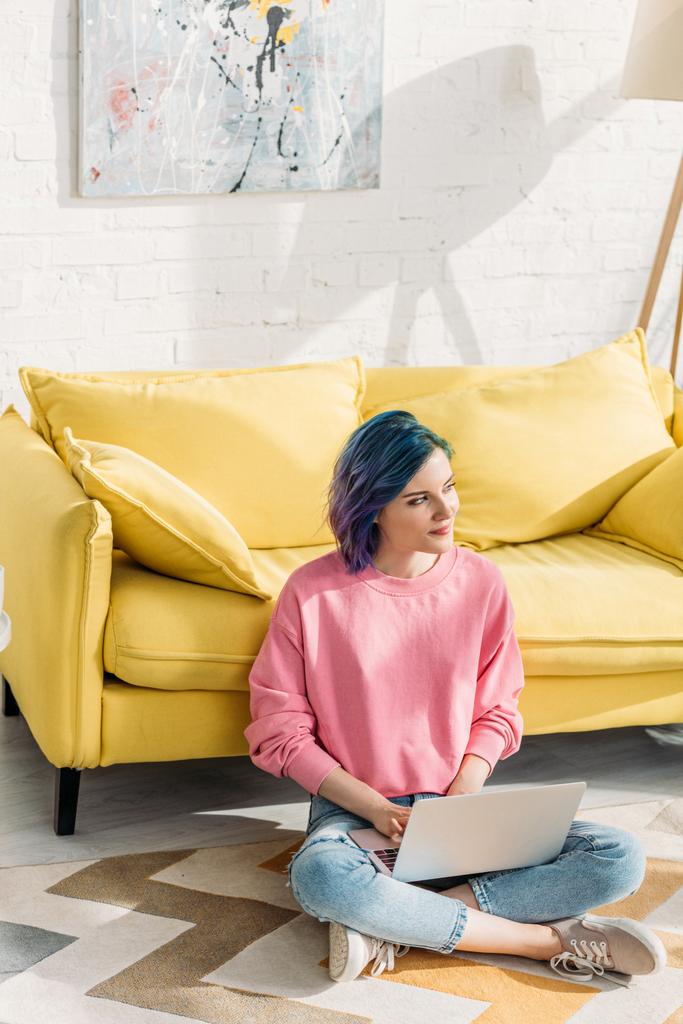 Korkea kulma näkymä harkittuja freelancer värikkäitä hiuksia katselee pois ja työskentelee kannettavan tietokoneen lähellä sohva lattialla
  - Valokuva, kuva